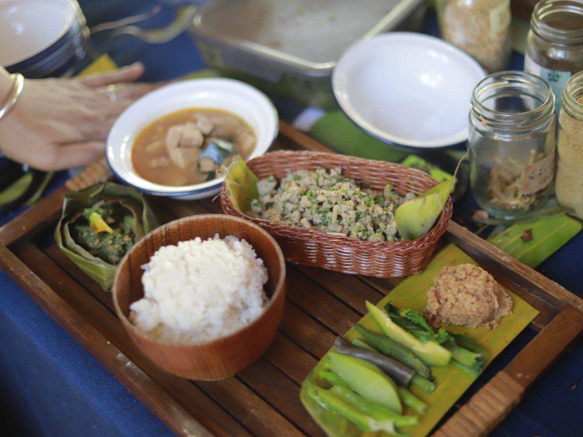 A Lanna meal on a wooden tray: rice, curry and herbs in woven baskets
