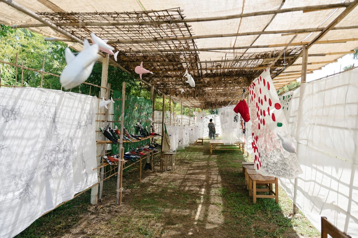 Hand-stitched textile pieces and soft toys hanging along a bamboo-covered walkway at SEN