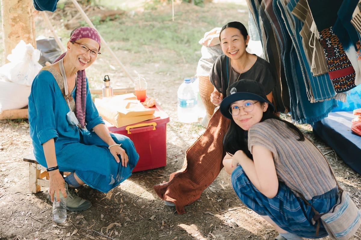Three women sharing a laugh beside hand-woven textiles at SEN