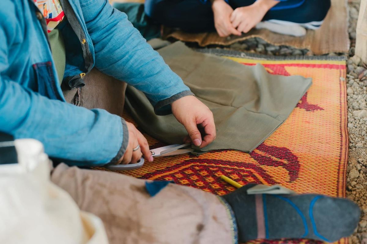 Hands cutting fabric on a woven mat during a craft workshop