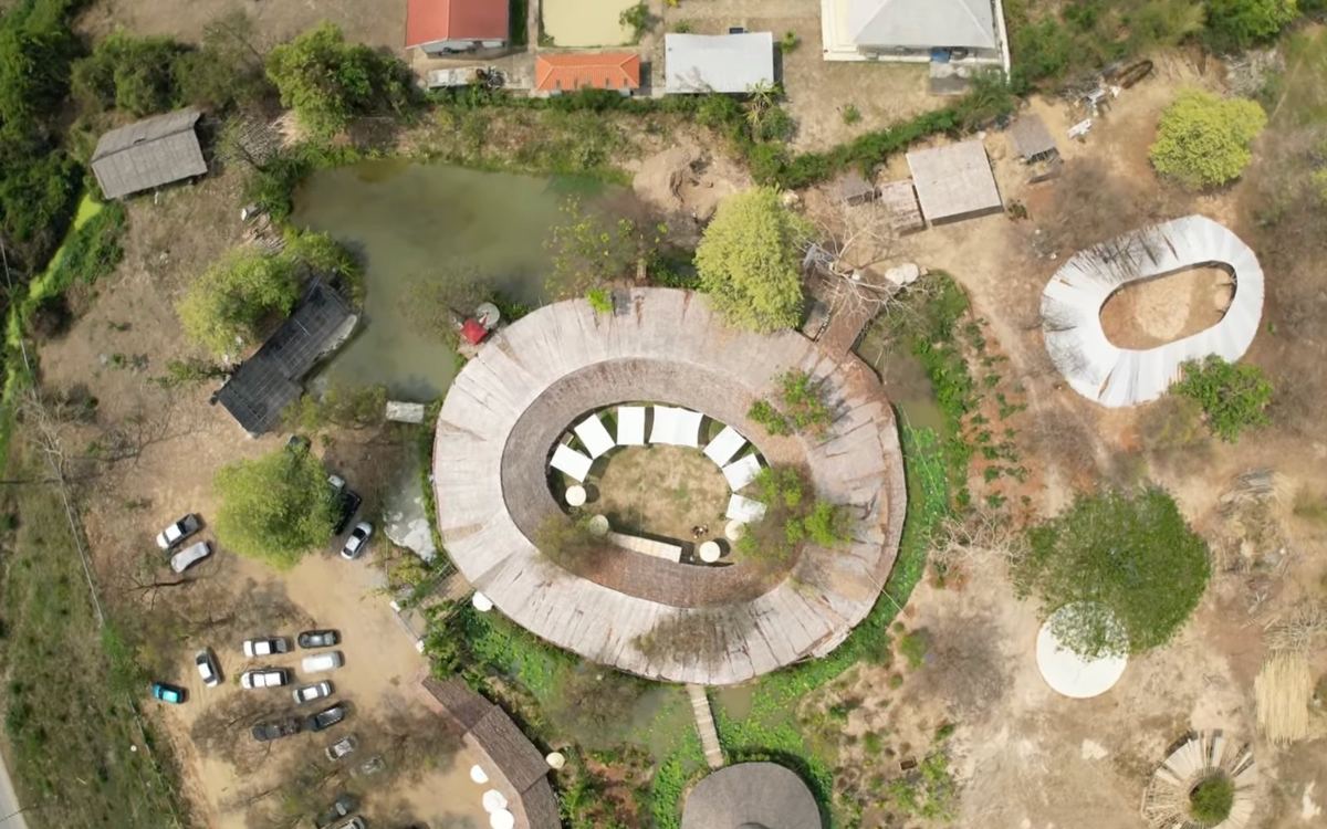The courtyard from above: an oval bamboo roof around white umbrellas, with the pond and gardens