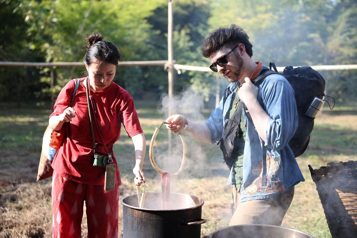 Two visitors lifting yarn from a steaming natural-dye pot