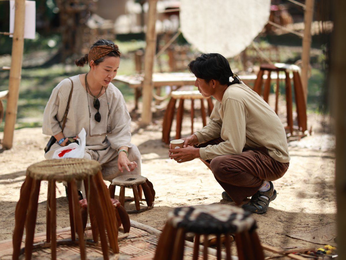 A maker and a visitor in conversation over handmade stools