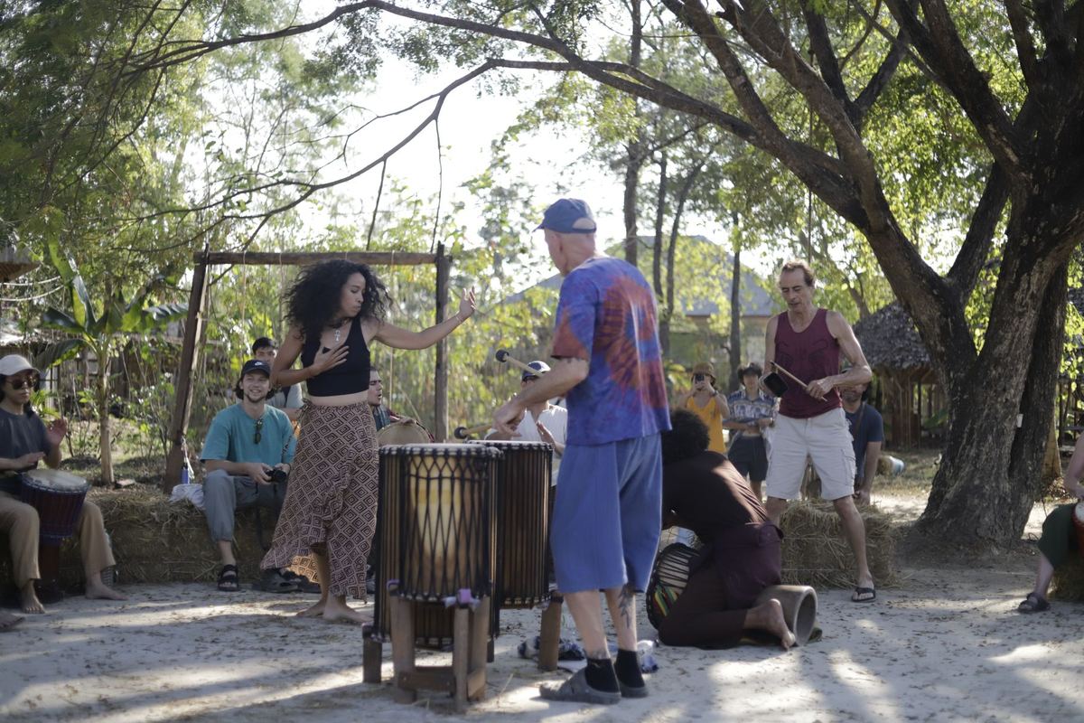 The drum circle under the trees: drummers, a dancer and listeners on hay bales