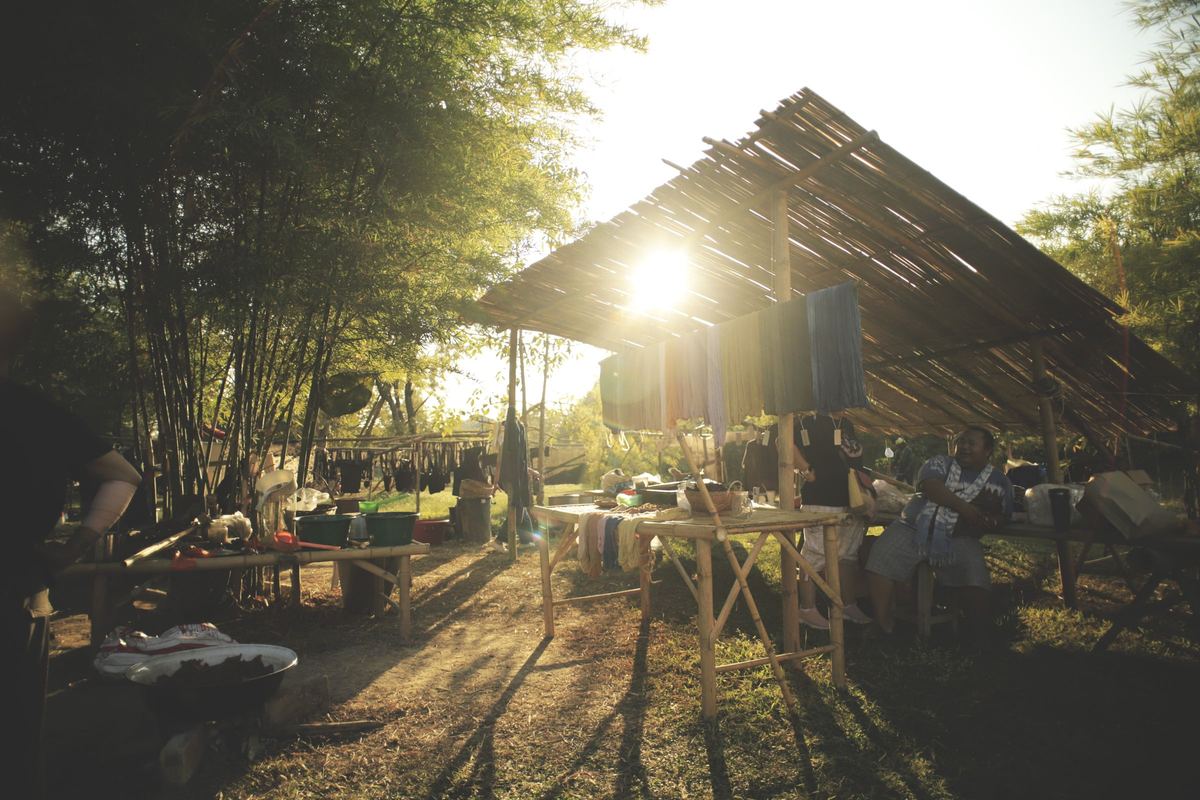 The dye shed and market tables in the late sun, dyed cloth drying under a bamboo roof