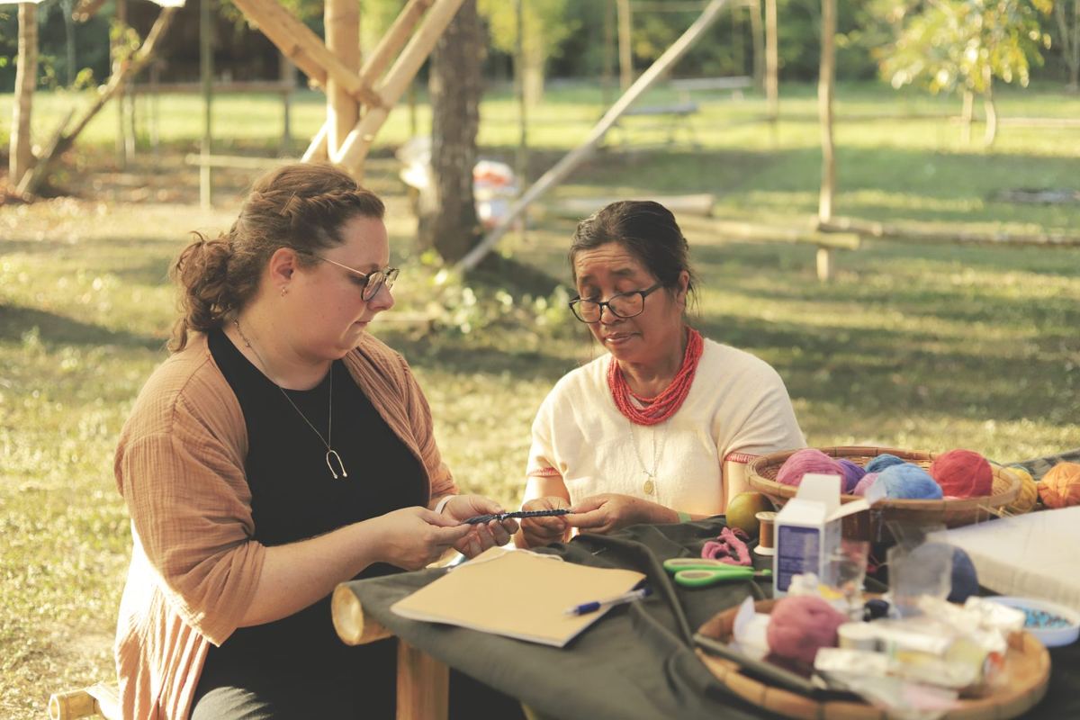 Two women examining a braided thread at a weaving table