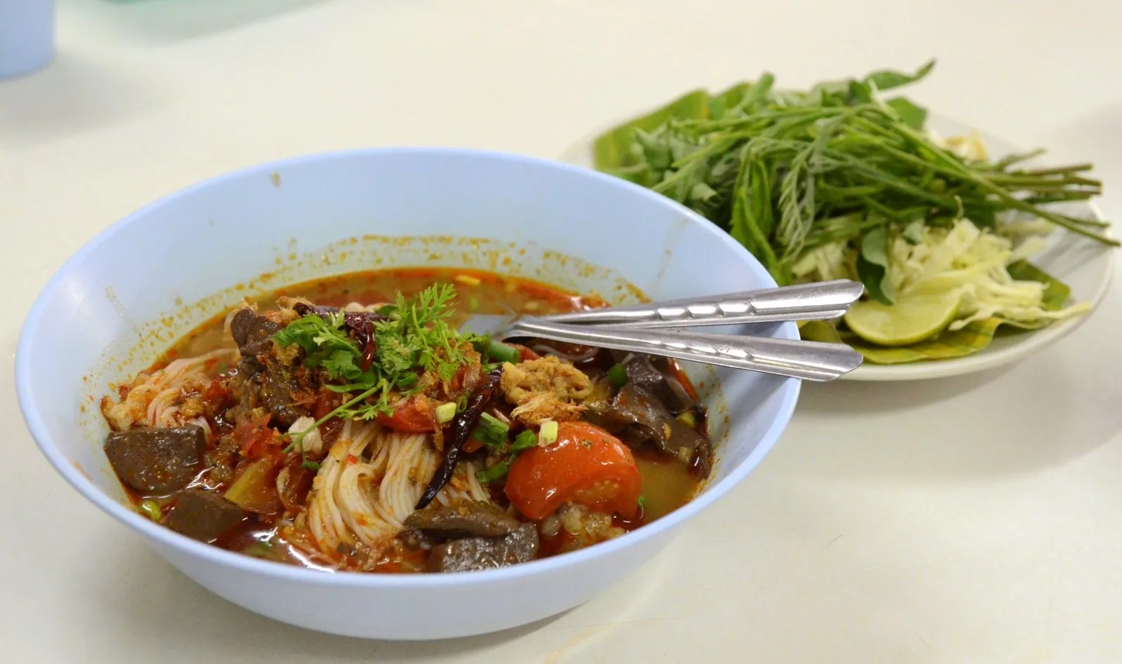 A bowl of khanom jeen nam ngiao, rice noodles in a spicy tomato broth
