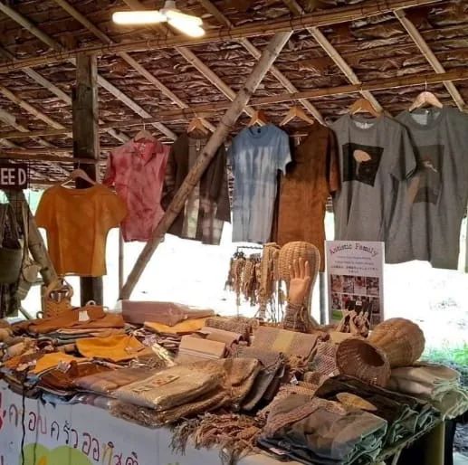 Naturally tie-dyed shirts hanging above woven bags and baskets at the AuJaa’ Craft stall